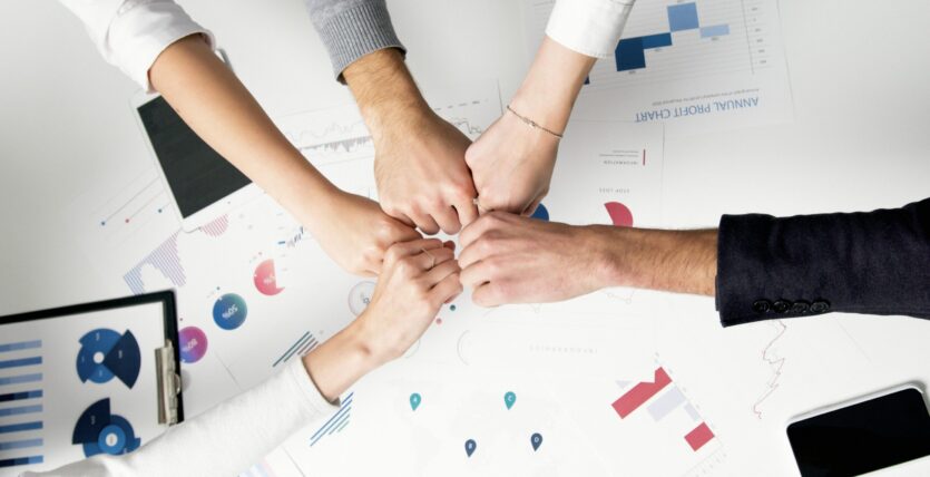 Free Colleagues celebrate success with a fist bump over financial charts depicting teamwork and unity. Stock Photo
