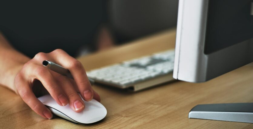 Free A hand using a wireless mouse at a modern desk setup with a computer and keyboard. Stock Photo